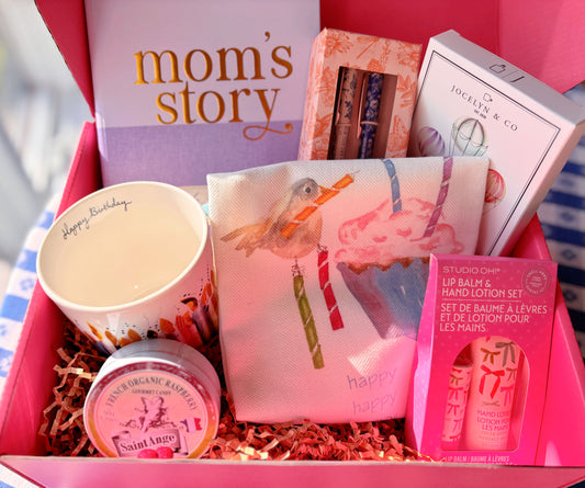 The Birthday Celebration Gift Box from Lifts & Gifts, showing the Mom's Story Keepsake Journal, a Jane Austin Pen & Pencil Set, a Happy Birthday Ceramic Mug, a Birthday-Cake-n-a-Mug to make, a Cotton Birthday Tea Towel, a  Lip Balm & Hand Lotion Set, and a Decorative Tin of Raspberry Birthday Candies.