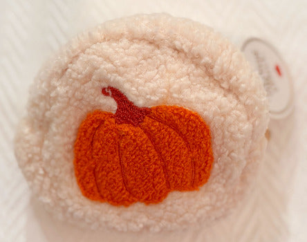 A close-up of a ivory-colored, fuzzy teddy pouch featuring an orange pumpkin applique with a dark red stem on the front. Perfect for carrying accessories.